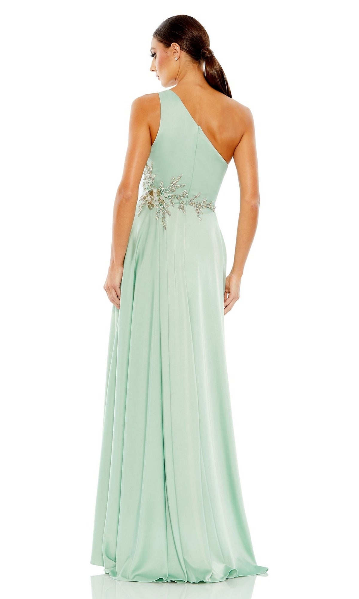 A woman stands with her back to the camera, wearing the Long Formal Dress 11262 by Mac Duggal—a light green pastel one-shoulder gown featuring an embellished waist.